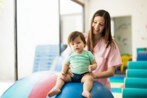 baby on top of an exercise ball being steadied by his therapist