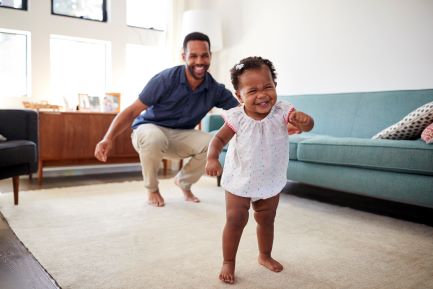 young girl learning to walk while her dad follows behind