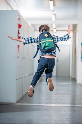 child wearing a backpack jumping and running in a school hallway