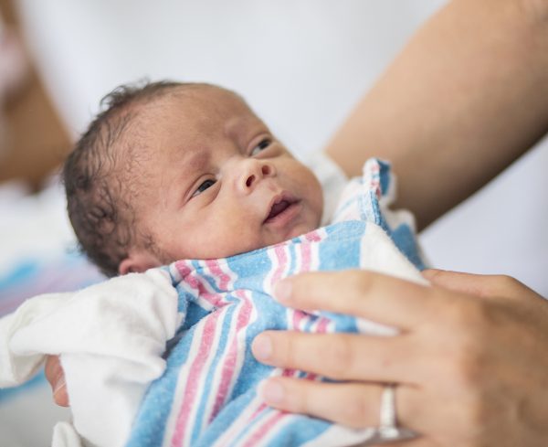 newborn baby in a hospital blanket being held by an adult