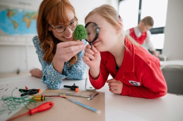 child using a magnifying glass to inspect a miniature tree being held by her therapist